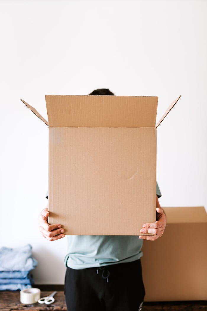 Faceless individual holding an open cardboard box during a home move.